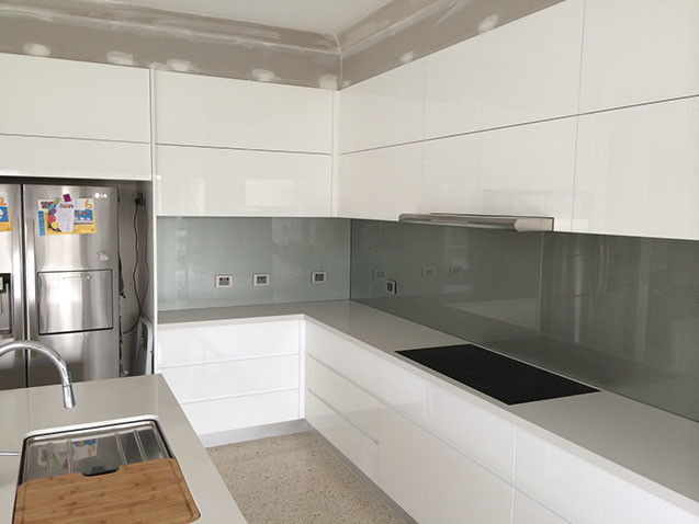 Medium sized contemporary l-shaped kitchen/diner in Perth with a submerged sink, flat-panel cabinets, white cabinets, granite worktops, grey splashback, glass sheet splashback, stainless steel appliances, concrete flooring and an island.