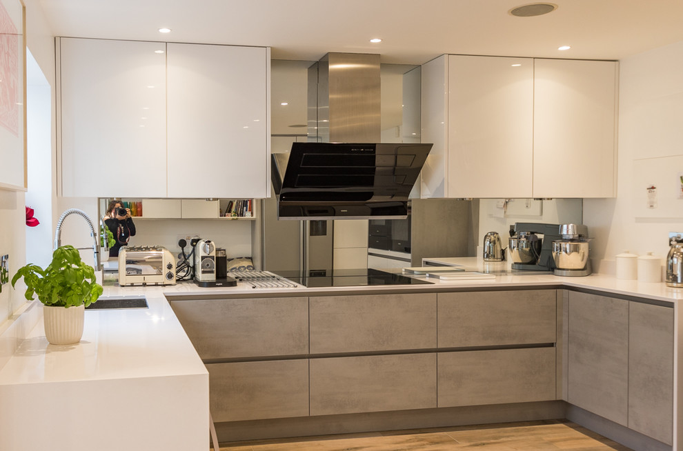 Bild på ett mellanstort funkis kök, med en integrerad diskho, släta luckor, grå skåp, bänkskiva i kvartsit, stänkskydd med metallisk yta, spegel som stänkskydd, rostfria vitvaror, ljust trägolv och brunt golv