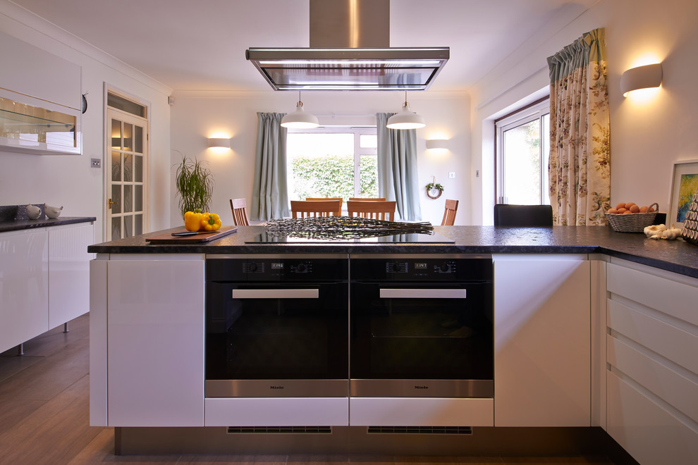 Photo of a small contemporary u-shaped kitchen/diner in Buckinghamshire with a double-bowl sink, flat-panel cabinets, white cabinets, granite worktops, stainless steel appliances and porcelain flooring.