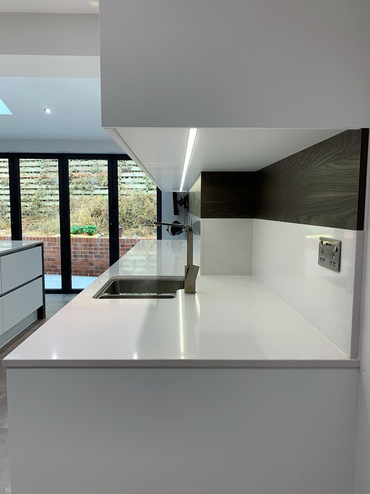 Design ideas for a medium sized contemporary l-shaped open plan kitchen in Other with a single-bowl sink, flat-panel cabinets, dark wood cabinets, composite countertops, white splashback, stainless steel appliances, vinyl flooring, an island and white worktops.