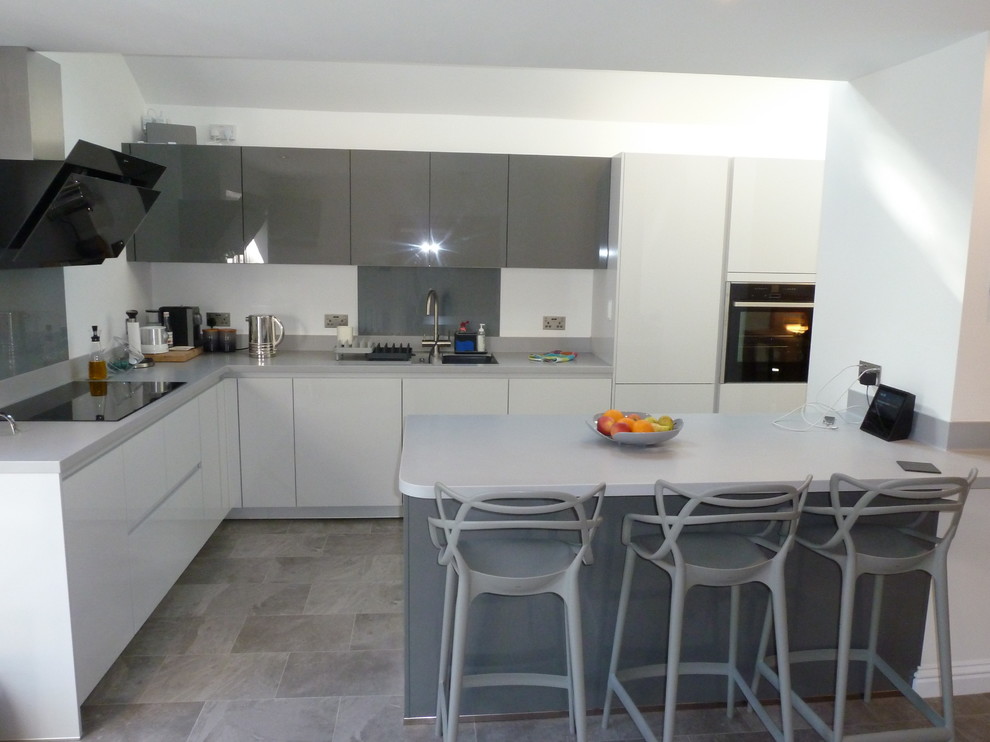 Modern inredning av ett mellanstort grå grått kök, med en nedsänkt diskho, släta luckor, grå skåp, bänkskiva i koppar, grått stänkskydd, glaspanel som stänkskydd, svarta vitvaror, linoleumgolv, en köksö och grått golv