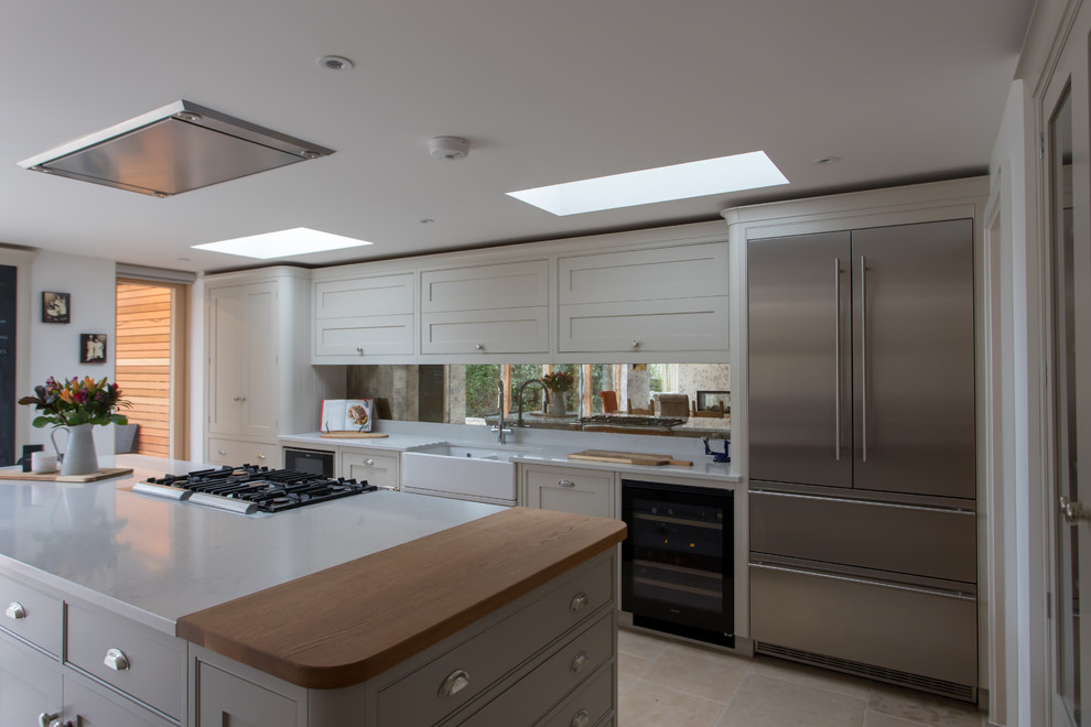 This is an example of an expansive classic u-shaped kitchen/diner in Hertfordshire with a belfast sink, shaker cabinets, grey cabinets, quartz worktops, metallic splashback, mirror splashback, stainless steel appliances, limestone flooring, an island, beige floors and yellow worktops.