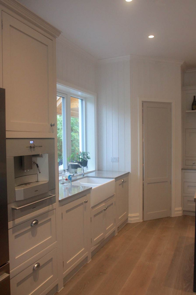 Photo of a medium sized traditional l-shaped kitchen/diner in Surrey with beaded cabinets, beige cabinets, black appliances, an island and grey worktops.