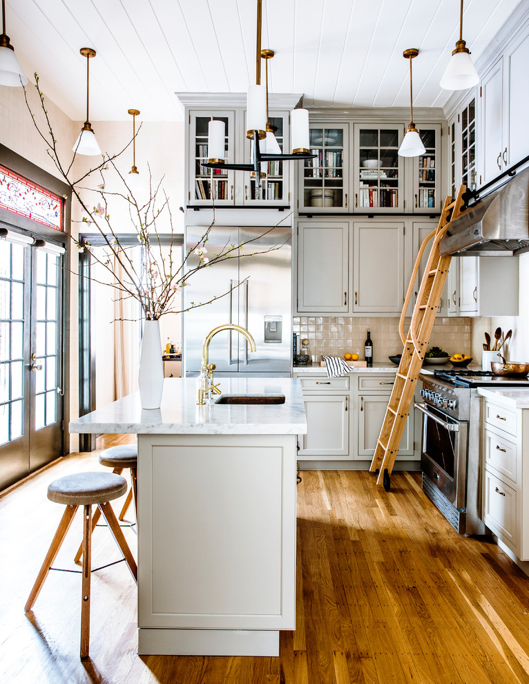 Foto på ett vintage l-kök, med grå skåp, marmorbänkskiva, vitt stänkskydd, stänkskydd i keramik, en köksö, en undermonterad diskho, luckor med infälld panel, rostfria vitvaror, mellanmörkt trägolv och brunt golv