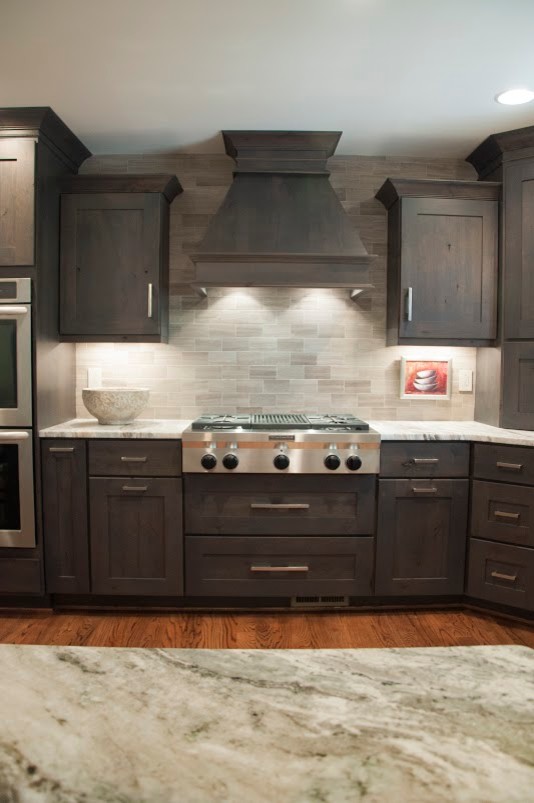 Mid-sized transitional l-shaped medium tone wood floor eat-in kitchen photo in Nashville with an undermount sink, shaker cabinets, dark wood cabinets, granite countertops, gray backsplash, stone tile backsplash, stainless steel appliances and an island