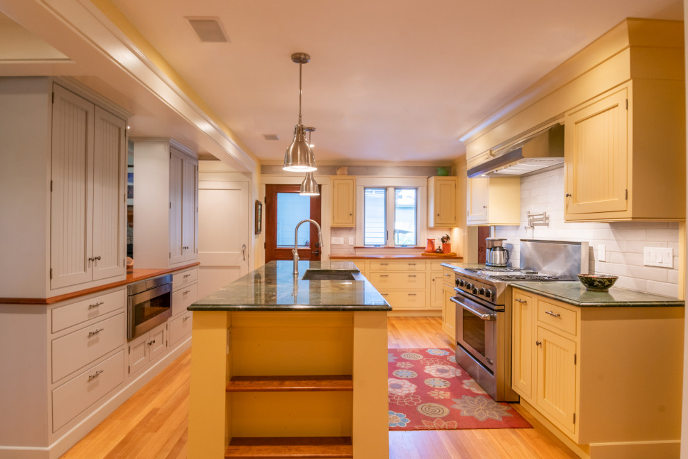 Enclosed kitchen - mid-sized country light wood floor and brown floor enclosed kitchen idea in Boston with a farmhouse sink, beaded inset cabinets, yellow cabinets, granite countertops, white backsplash, subway tile backsplash, stainless steel appliances, an island and green countertops