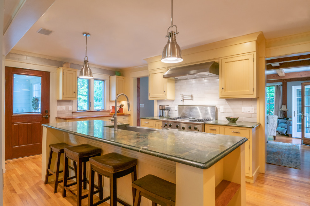 ボストンにある高級な中くらいなカントリー風のおしゃれなキッチン (エプロンフロントシンク、インセット扉のキャビネット、黄色いキャビネット、御影石カウンター、白いキッチンパネル、サブウェイタイルのキッチンパネル、シルバーの調理設備、淡色無垢フローリング、茶色い床、緑のキッチンカウンター) の写真