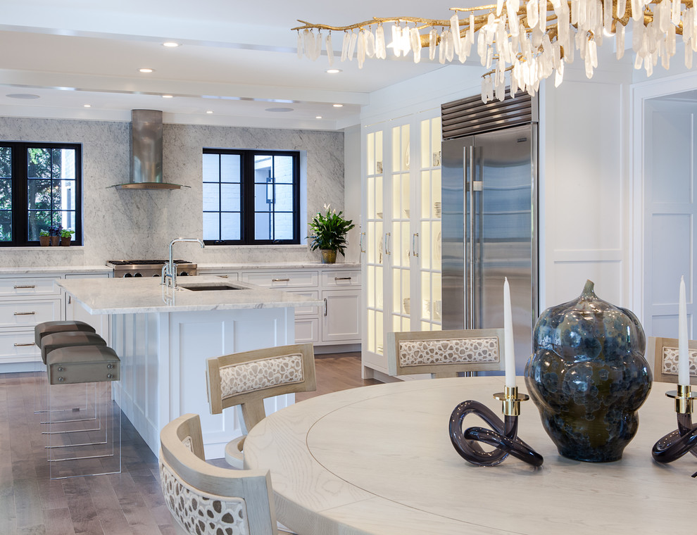 Example of a large transitional l-shaped dark wood floor and brown floor eat-in kitchen design in Boston with an undermount sink, glass-front cabinets, white cabinets, marble countertops, gray backsplash, marble backsplash, stainless steel appliances, an island and white countertops