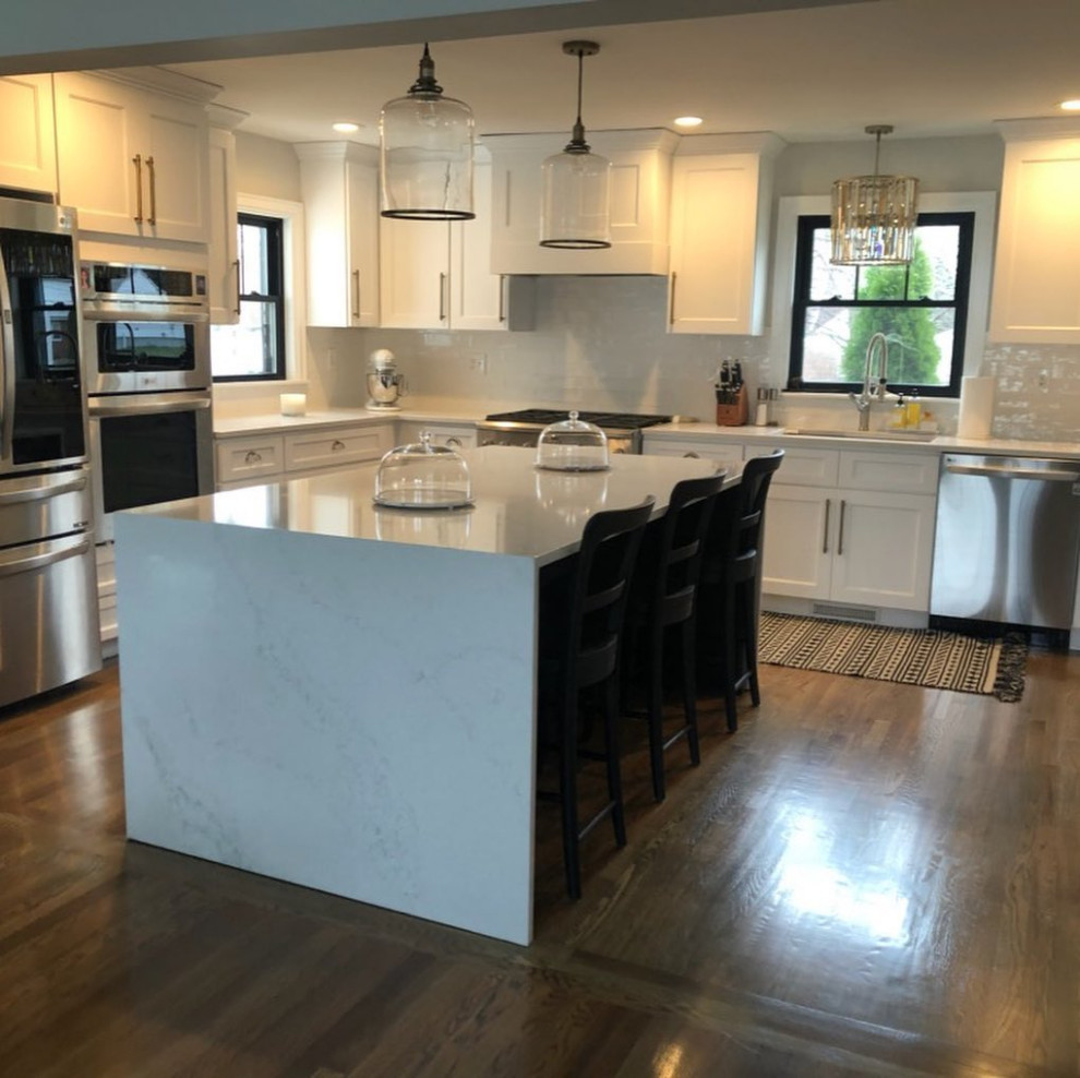 Bild på ett mellanstort funkis vit vitt kök, med en undermonterad diskho, skåp i shakerstil, vita skåp, bänkskiva i kvarts, vitt stänkskydd, stänkskydd i porslinskakel, rostfria vitvaror, mellanmörkt trägolv och en köksö