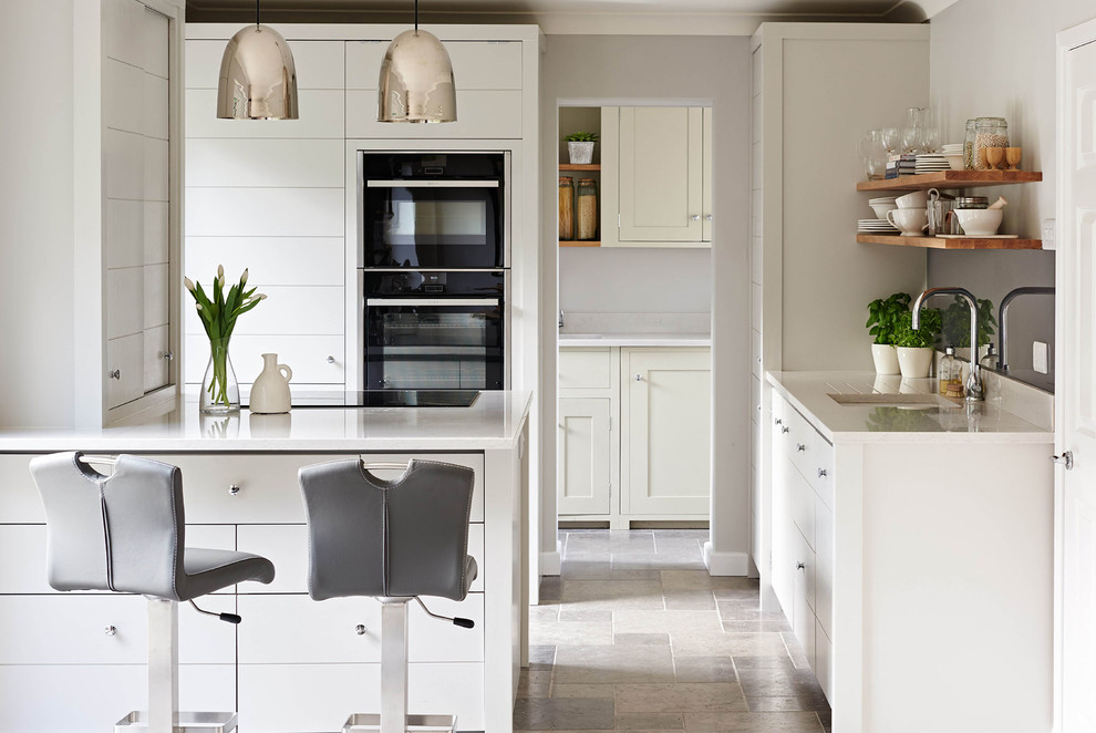 Idéer för att renovera ett mellanstort, avskilt funkis l-kök, med en undermonterad diskho, vita skåp, marmorbänkskiva, kalkstensgolv, en halv köksö, släta luckor, svarta vitvaror och grått golv