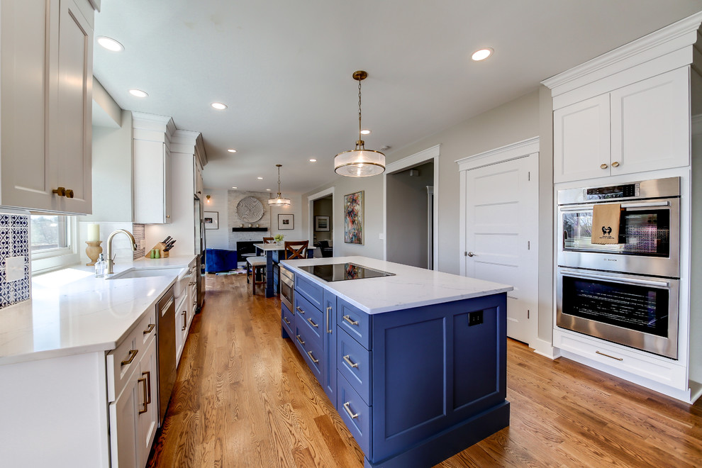 Klassisk inredning av ett stort vit vitt kök, med en rustik diskho, luckor med infälld panel, blå skåp, bänkskiva i kvartsit, flerfärgad stänkskydd, stänkskydd i cementkakel, rostfria vitvaror, ljust trägolv, flera köksöar och brunt golv