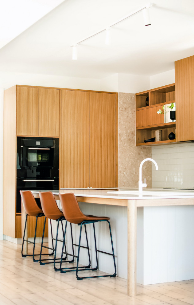 This is an example of a scandinavian l-shaped kitchen in Melbourne with flat-panel cabinets, medium wood cabinets, black appliances, light hardwood flooring, an island, beige floors and white worktops.