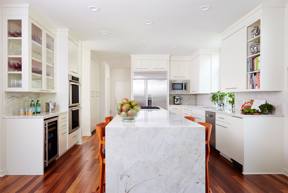 Contemporary u-shaped kitchen in Minneapolis with flat-panel cabinets, white cabinets, stainless steel appliances, an island, white worktops, a submerged sink, white splashback, medium hardwood flooring and brown floors.