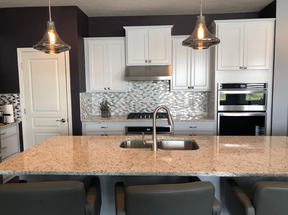 Small vintage l-shaped open plan kitchen in Indianapolis with recessed-panel cabinets, white cabinets, granite worktops, multi-coloured splashback, mosaic tiled splashback, stainless steel appliances, vinyl flooring, an island, brown floors and white worktops.