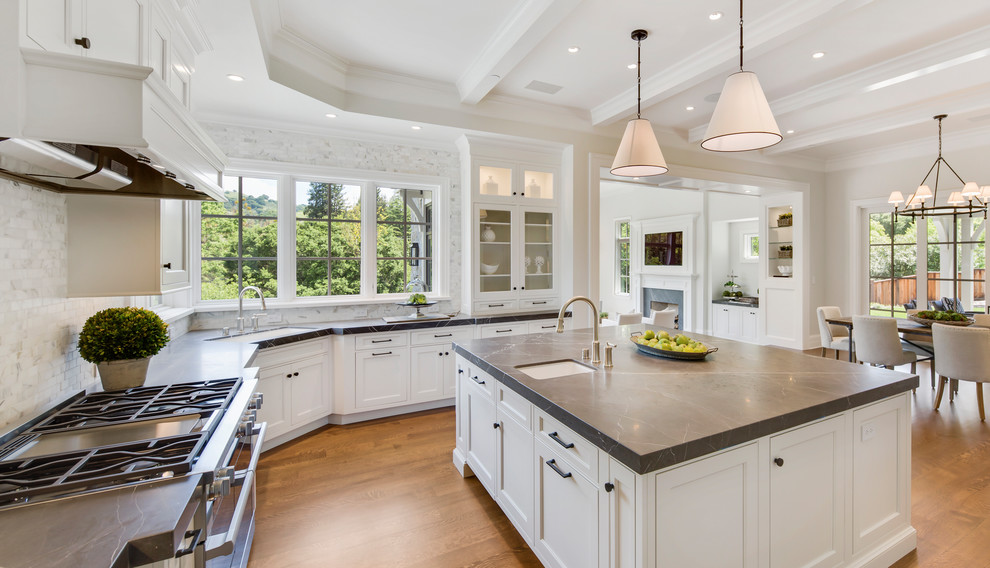 This is an example of a large classic u-shaped kitchen/diner in San Francisco with an island, glass-front cabinets, white cabinets, grey splashback, marble splashback, black worktops, a submerged sink, stainless steel appliances, medium hardwood flooring, brown floors and soapstone worktops.