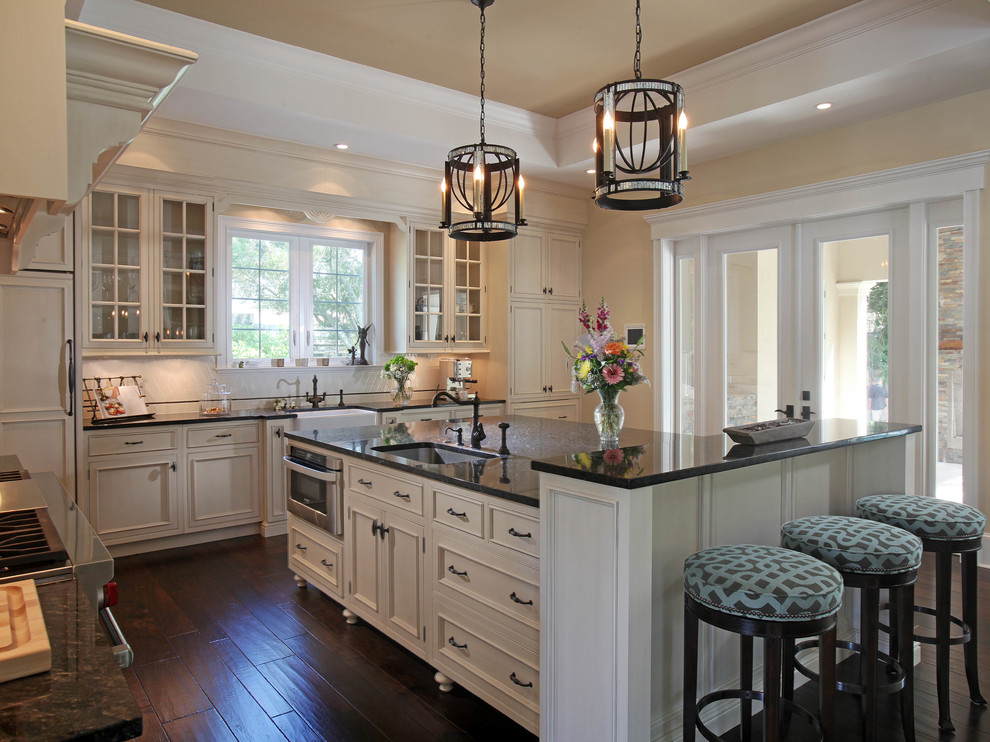 Mid-sized transitional l-shaped dark wood floor eat-in kitchen photo in Tampa with an undermount sink, glass-front cabinets, white cabinets, granite countertops, stainless steel appliances, an island, white backsplash and ceramic backsplash