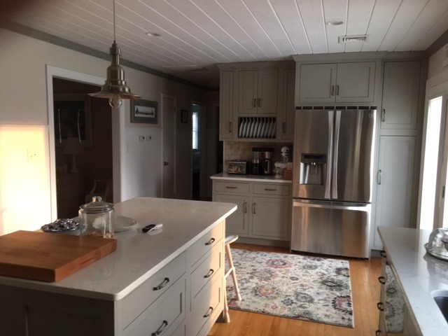 Klassisk inredning av ett mellanstort kök, med en undermonterad diskho, luckor med profilerade fronter, grå skåp, bänkskiva i kvartsit, grått stänkskydd, stänkskydd i tunnelbanekakel, rostfria vitvaror, ljust trägolv, en köksö och brunt golv