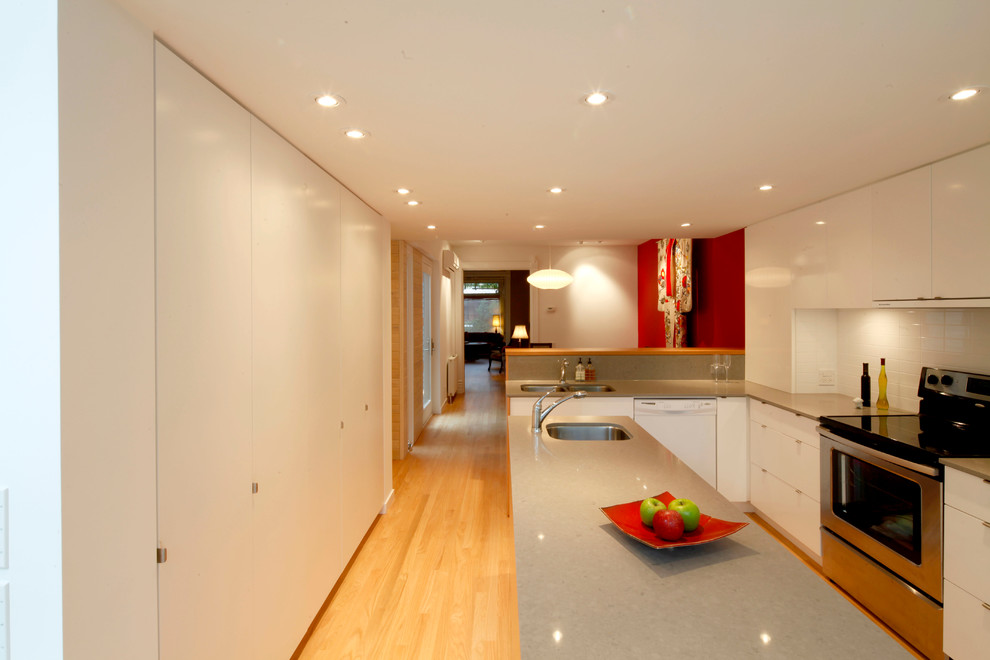 Photo of a contemporary galley kitchen/diner in Toronto with a submerged sink, flat-panel cabinets, white cabinets, engineered stone countertops, white splashback, metro tiled splashback and stainless steel appliances.