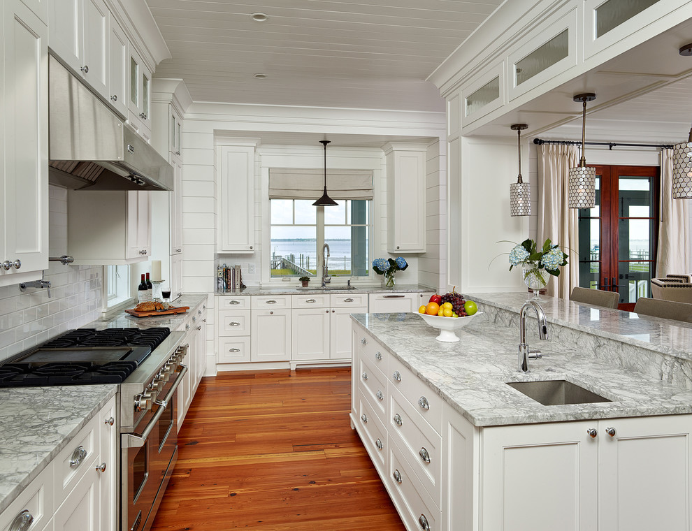 Inspiration for a coastal medium tone wood floor eat-in kitchen remodel in Charleston with an undermount sink, recessed-panel cabinets, white cabinets, white backsplash, subway tile backsplash, stainless steel appliances and granite countertops
