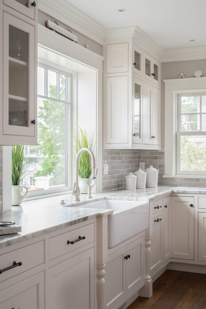 Inredning av ett klassiskt stort grå grått kök, med en rustik diskho, luckor med profilerade fronter, vita skåp, marmorbänkskiva, grått stänkskydd, stänkskydd i tunnelbanekakel, rostfria vitvaror och en köksö