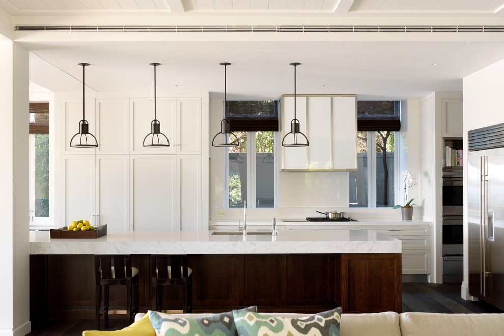 Exempel på ett mellanstort klassiskt kök, med en undermonterad diskho, luckor med infälld panel, rostfria vitvaror, vita skåp, marmorbänkskiva, vitt stänkskydd, glaspanel som stänkskydd, en köksö och mörkt trägolv