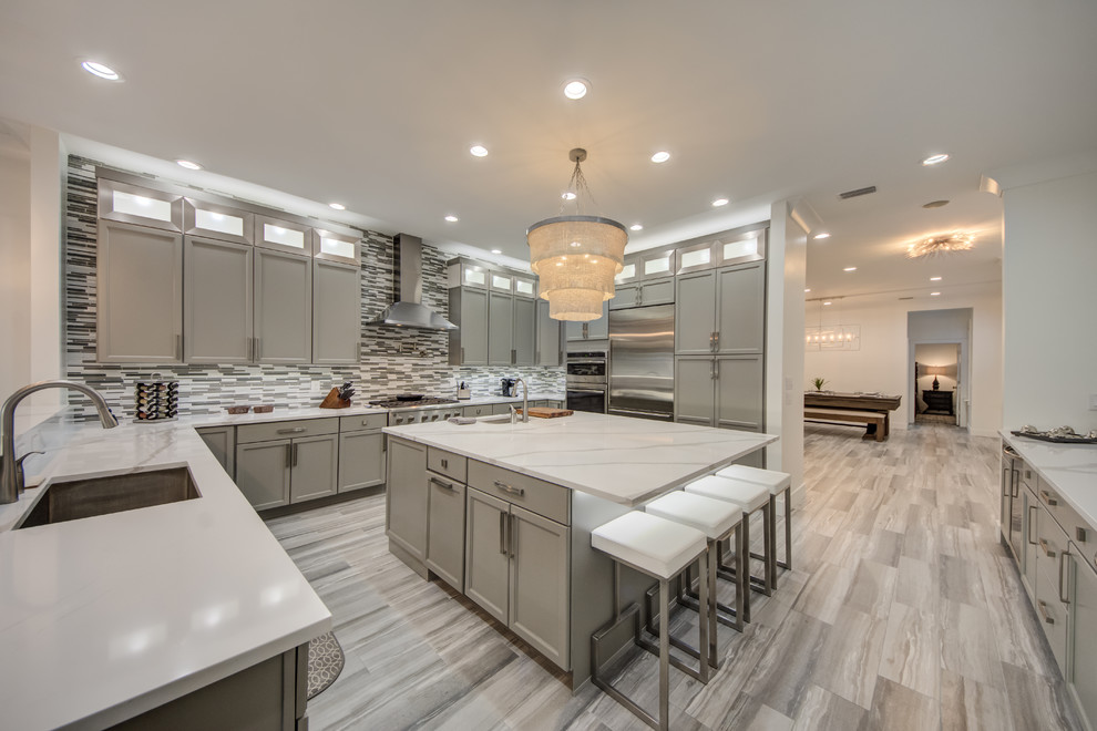 Photo of a classic u-shaped kitchen in Tampa with a submerged sink, recessed-panel cabinets, grey cabinets, grey splashback, stainless steel appliances, an island, grey floors and white worktops.