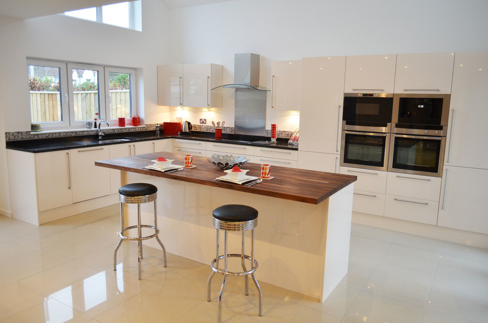 Exempel på ett mellanstort kök, med en enkel diskho, släta luckor, vita skåp, träbänkskiva, stänkskydd med metallisk yta, stänkskydd i metallkakel, rostfria vitvaror, klinkergolv i porslin och en köksö