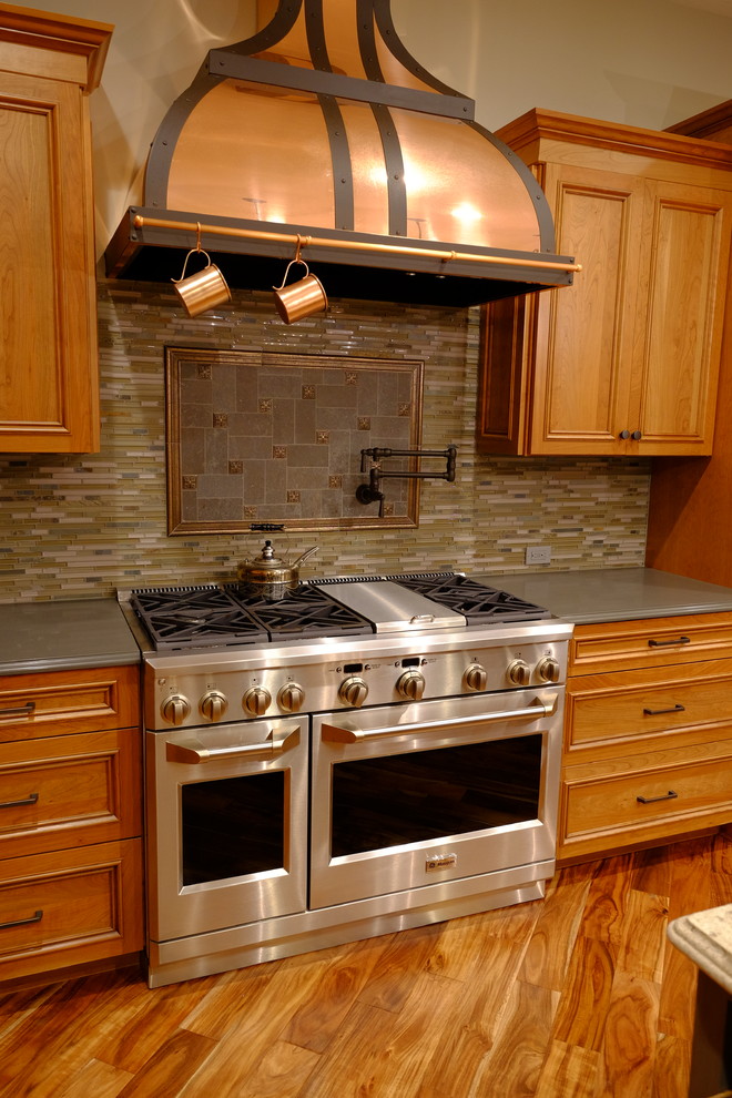Foto på ett stort amerikanskt l-kök, med en rustik diskho, luckor med upphöjd panel, skåp i mellenmörkt trä, bänkskiva i kvarts, grått stänkskydd, stänkskydd i glaskakel, rostfria vitvaror, mellanmörkt trägolv, en köksö och brunt golv