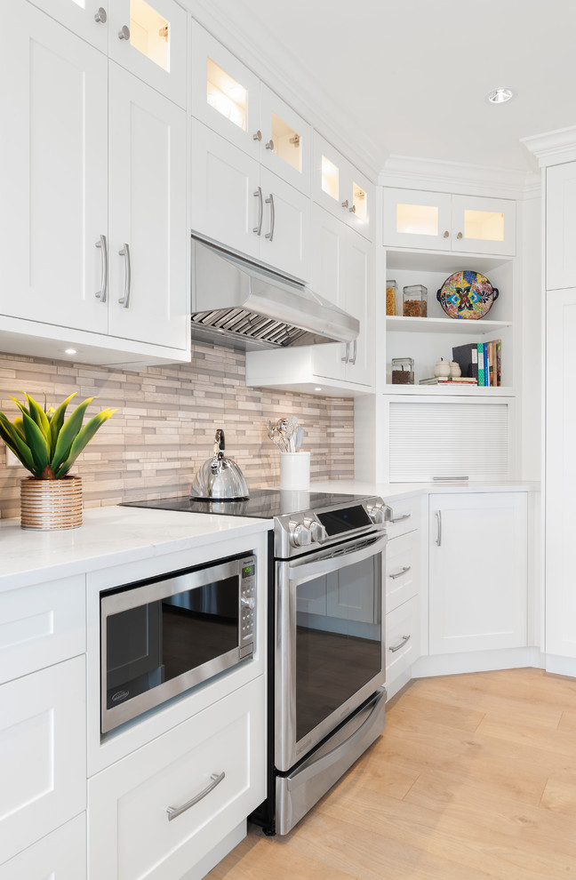 Eat-in kitchen - mid-sized transitional l-shaped laminate floor eat-in kitchen idea in Vancouver with an undermount sink, shaker cabinets, white cabinets, quartz countertops, gray backsplash, glass tile backsplash, stainless steel appliances and an island