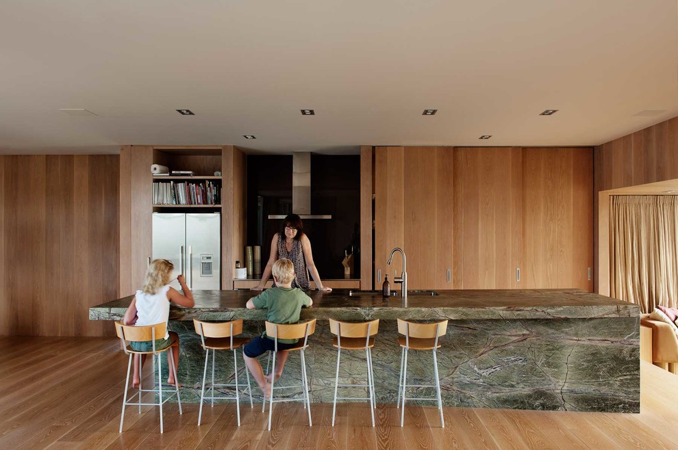 Zweizeilige Moderne Küche mit Doppelwaschbecken, flächenbündigen Schrankfronten, hellbraunen Holzschränken, Küchenrückwand in Schwarz, Küchengeräten aus Edelstahl, braunem Holzboden und Kücheninsel in Auckland