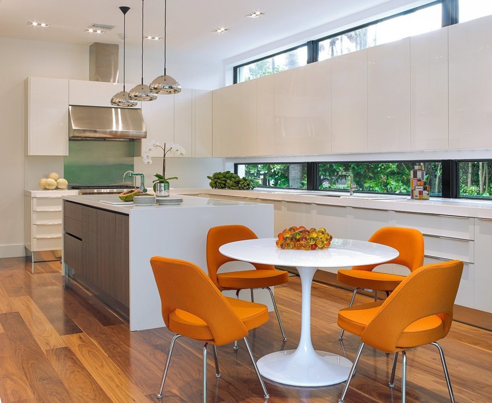 Große Moderne Wohnküche in L-Form mit Unterbauwaschbecken, flächenbündigen Schrankfronten, weißen Schränken, Küchengeräten aus Edelstahl, braunem Holzboden, Kücheninsel und Mineralwerkstoff-Arbeitsplatte in Miami