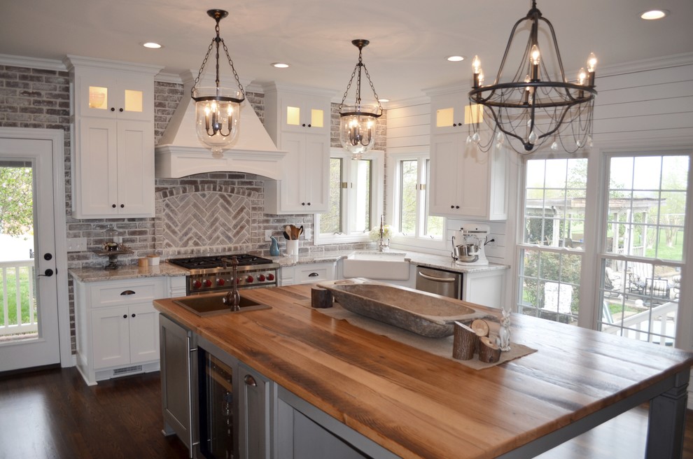 Example of a mid-sized country u-shaped medium tone wood floor and brown floor enclosed kitchen design in Nashville with a farmhouse sink, shaker cabinets, white cabinets, granite countertops, beige backsplash, brick backsplash, paneled appliances and an island