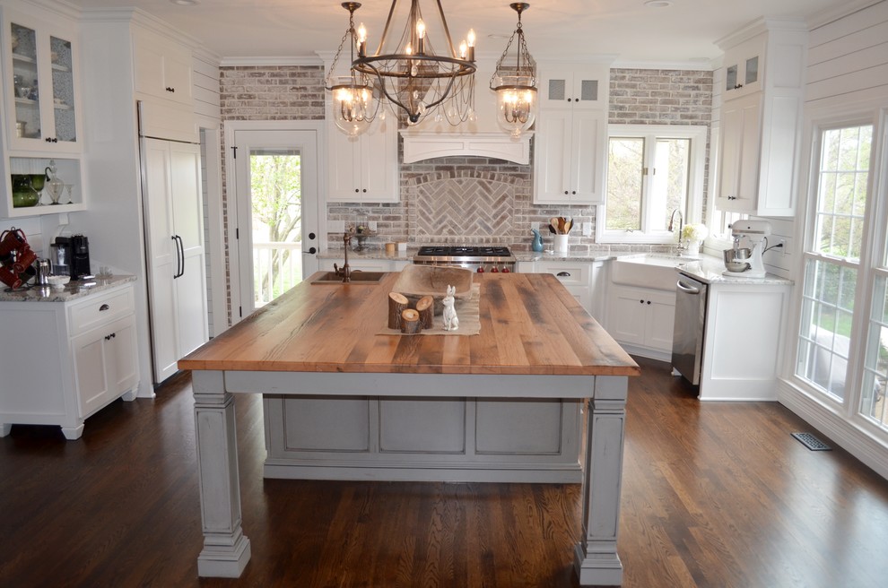 Mid-sized country u-shaped medium tone wood floor and brown floor enclosed kitchen photo in Nashville with a farmhouse sink, shaker cabinets, white cabinets, granite countertops, beige backsplash, brick backsplash, paneled appliances and an island