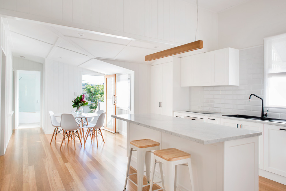 Modern inredning av ett mellanstort kök, med en nedsänkt diskho, vita skåp, marmorbänkskiva, vitt stänkskydd, stänkskydd i tunnelbanekakel, rostfria vitvaror, en köksö och ljust trägolv