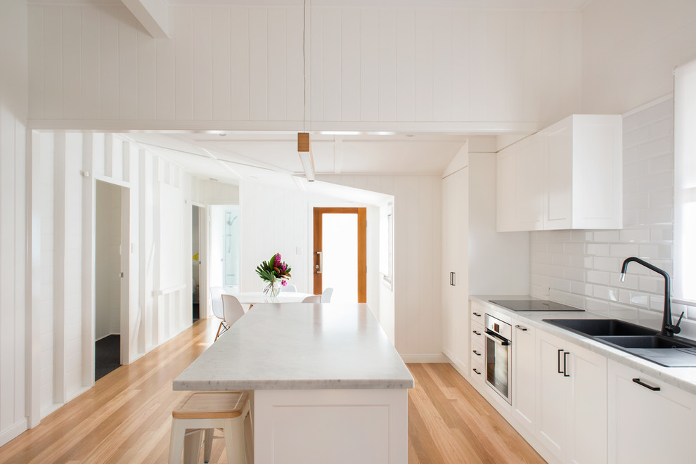 Bild på ett funkis kök, med en nedsänkt diskho, vita skåp, marmorbänkskiva, vitt stänkskydd, stänkskydd i tunnelbanekakel, rostfria vitvaror och en köksö