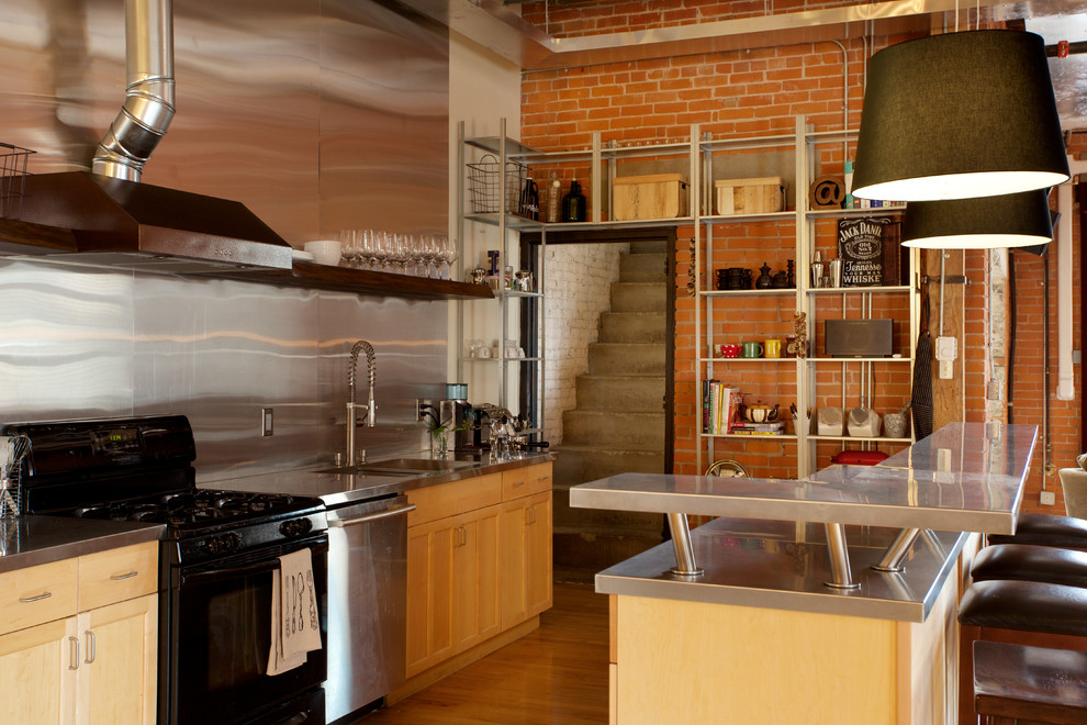 Urban galley open concept kitchen photo in Edmonton with light wood cabinets, stainless steel countertops, metal backsplash, black appliances and an island