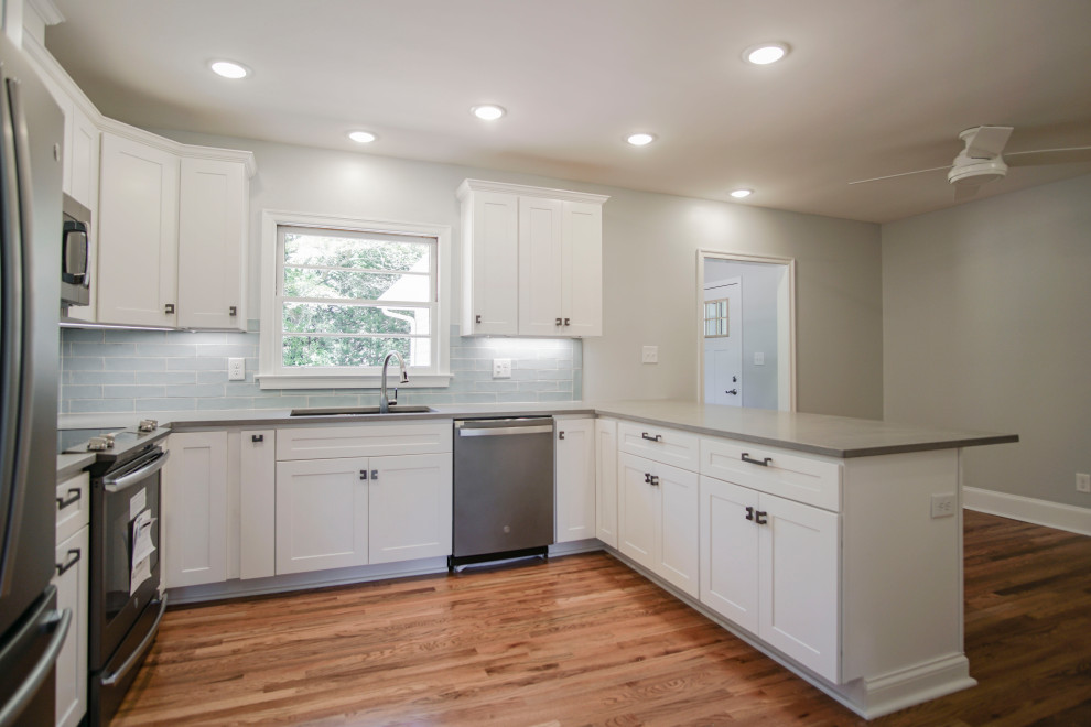 Inredning av ett klassiskt mellanstort grå grått kök, med en nedsänkt diskho, luckor med infälld panel, vita skåp, granitbänkskiva, blått stänkskydd, stänkskydd i keramik, rostfria vitvaror, ljust trägolv och brunt golv