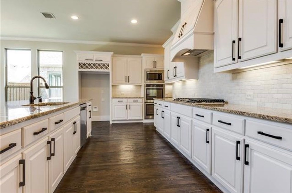 Inspiration for a mid-sized timeless single-wall dark wood floor and brown floor eat-in kitchen remodel in Dallas with an undermount sink, raised-panel cabinets, white cabinets, granite countertops, white backsplash, stone tile backsplash, an island, stainless steel appliances and beige countertops