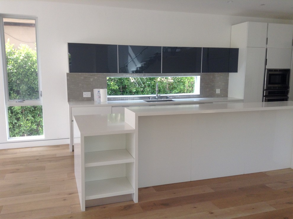 Immagine di una grande cucina minimal con ante lisce, ante bianche, paraspruzzi grigio e parquet chiaro