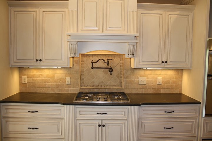 Inspiration for a timeless u-shaped enclosed kitchen remodel in Atlanta with raised-panel cabinets, distressed cabinets, granite countertops, beige backsplash, stone tile backsplash and an island