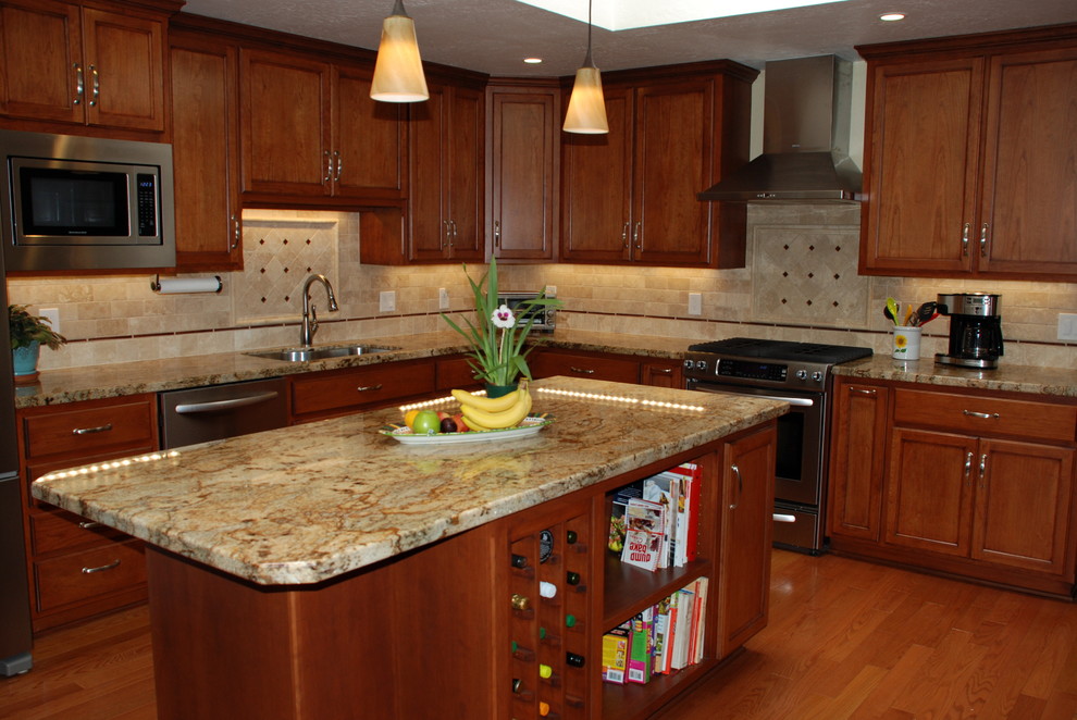 Bild på ett stort medelhavsstil kök, med en enkel diskho, luckor med infälld panel, skåp i mellenmörkt trä, granitbänkskiva, beige stänkskydd, stänkskydd i tunnelbanekakel, rostfria vitvaror, ljust trägolv och en köksö