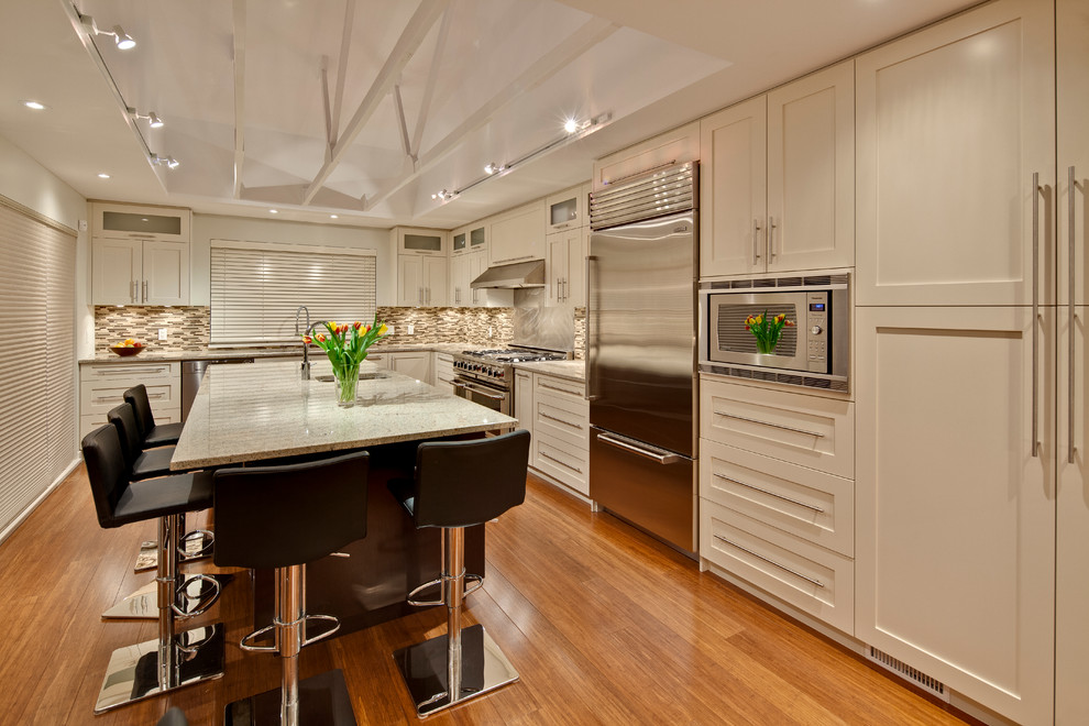 Large trendy l-shaped medium tone wood floor eat-in kitchen photo in Vancouver with an undermount sink, shaker cabinets, white cabinets, granite countertops, multicolored backsplash, mosaic tile backsplash, stainless steel appliances and an island