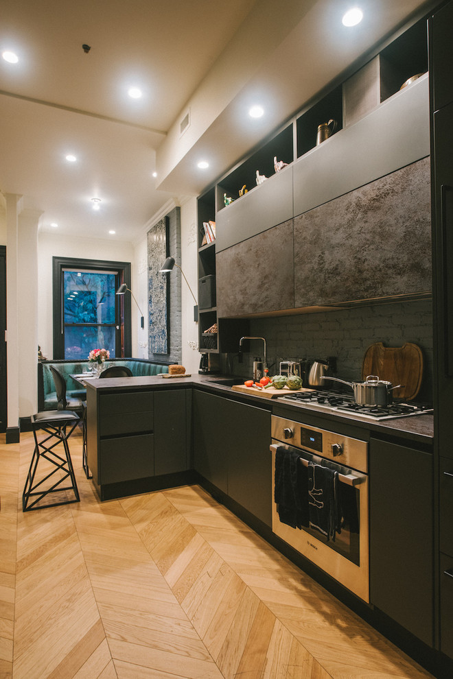 ニューヨークにあるインダストリアルスタイルのおしゃれなキッチン (フラットパネル扉のキャビネット、グレーのキャビネット、グレーのキッチンパネル、レンガのキッチンパネル、シルバーの調理設備、無垢フローリング、茶色い床、グレーのキッチンカウンター) の写真