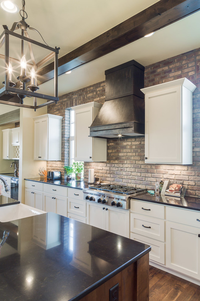 Example of a mid-sized farmhouse l-shaped medium tone wood floor kitchen pantry design in Denver with a farmhouse sink, recessed-panel cabinets, white cabinets, quartzite countertops, brown backsplash, stainless steel appliances, an island and subway tile backsplash