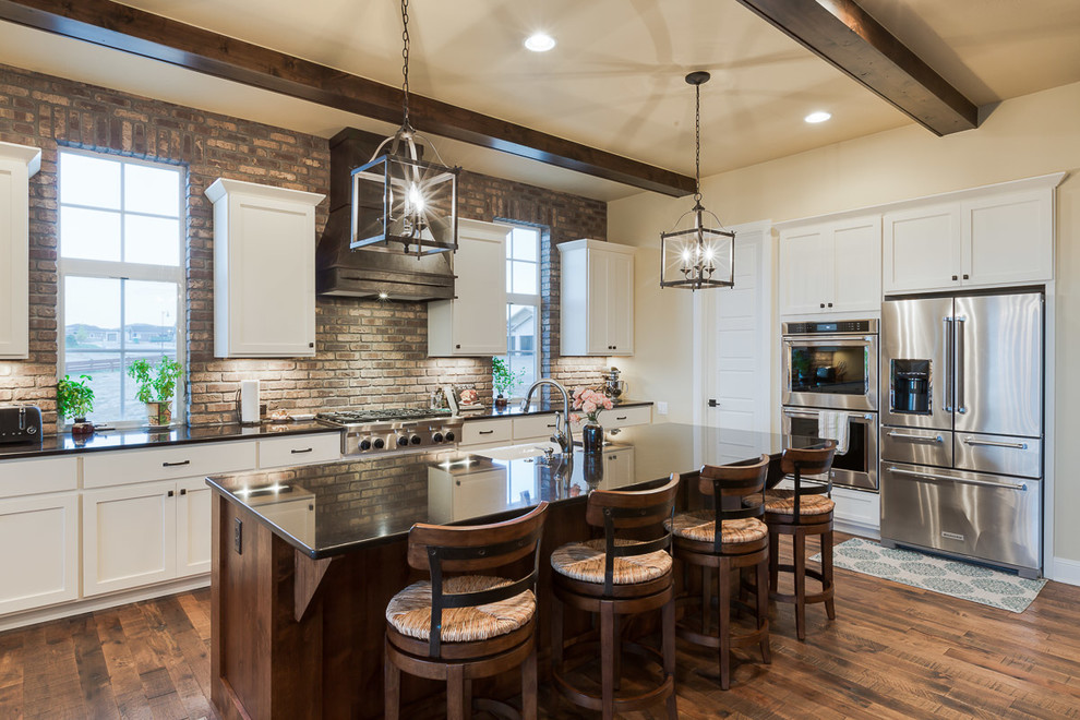 Example of a mid-sized country l-shaped medium tone wood floor kitchen design in Denver with a farmhouse sink, recessed-panel cabinets, white cabinets, quartzite countertops, brown backsplash, subway tile backsplash, stainless steel appliances and an island