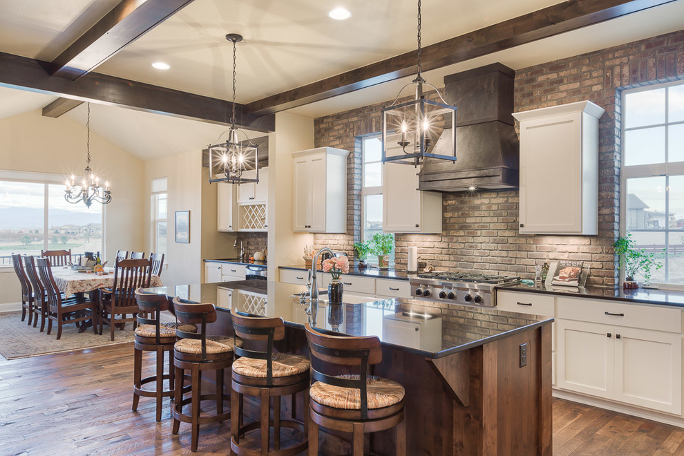 Example of a mid-sized farmhouse galley medium tone wood floor eat-in kitchen design in Denver with recessed-panel cabinets, white cabinets, quartzite countertops, brown backsplash, stainless steel appliances, an island and stone tile backsplash