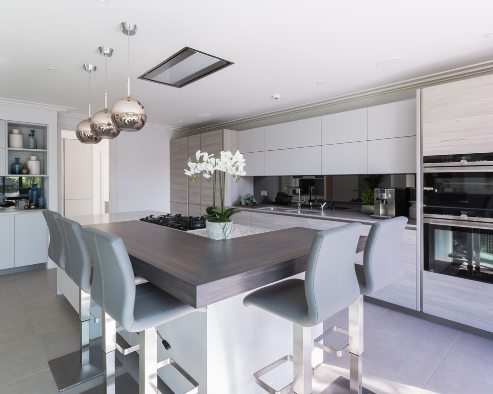 Inspiration for a large contemporary l-shaped kitchen/diner in Gloucestershire with a submerged sink, flat-panel cabinets, light wood cabinets, composite countertops, metallic splashback, mirror splashback, stainless steel appliances, porcelain flooring, an island, grey floors and multicoloured worktops.