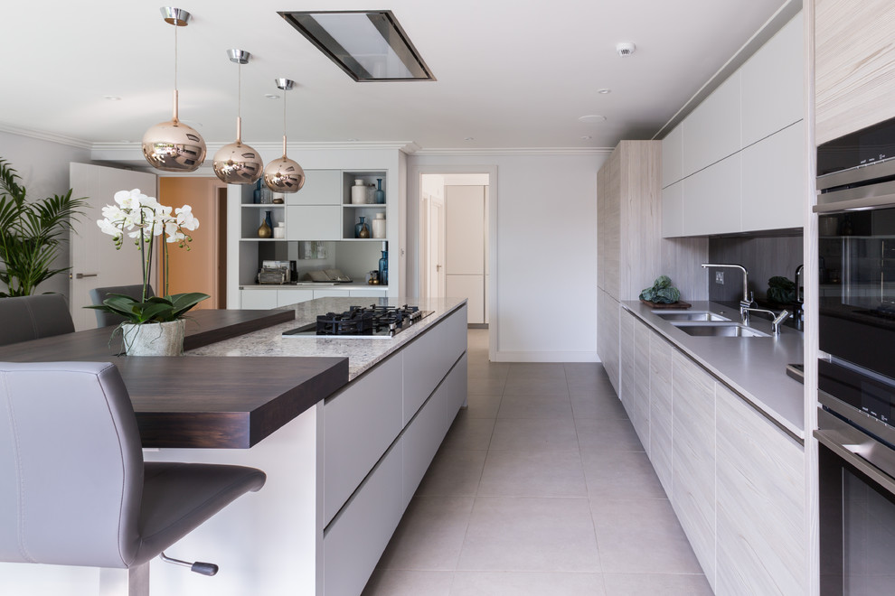 This is an example of a large contemporary l-shaped kitchen/diner in Gloucestershire with a submerged sink, flat-panel cabinets, light wood cabinets, composite countertops, metallic splashback, mirror splashback, stainless steel appliances, porcelain flooring, an island, grey floors and multicoloured worktops.