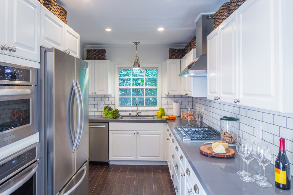 Klassische Küche in U-Form mit Unterbauwaschbecken, profilierten Schrankfronten, weißen Schränken, Küchenrückwand in Weiß, Rückwand aus Metrofliesen und dunklem Holzboden in Los Angeles