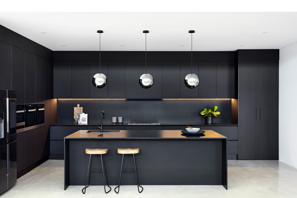 Photo of a large contemporary galley kitchen in Sydney with a submerged sink, flat-panel cabinets, black cabinets, concrete flooring, grey floors, black worktops, engineered stone countertops, black splashback, stone slab splashback, stainless steel appliances and no island.